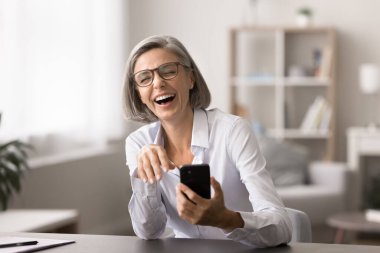 Mutlu iş kadını gülüyor, modern akıllı telefonla masaya oturuyor, satış hedefine ulaşıyor, terfi ya da ikramiye hakkında harika haberler alıyor, olumlu müvekkil yorumları yapıyor, meslektaşlarından komik espriler alıyor.