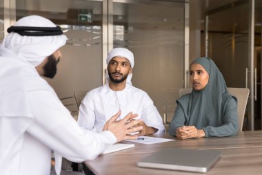 Müslüman başlıklı kadın ve erkek Arap iş ortakları büyük ofis masasında konuşuyor, proje, işbirliği, takım çalışması, şirket yatırımları için çözümler tartışıyorlar.