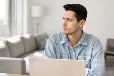 Ciddi düşünceli genç Latin serbest girişimci evde dizüstü bilgisayarda çalışıyor, derin düşüncelere dalmış, iş projesi için çözümler düşünüyor, problem çözme stratejisi geliştiriyor.