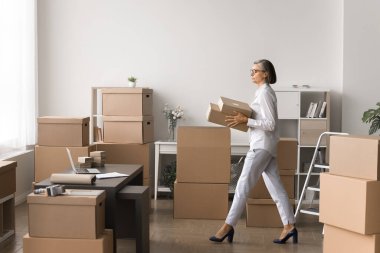 Yaşlı bir kadın depoda küçük kutular taşıyor, paketleri taşıyor, yönetiyor ve taşıyor, emir komuta ve planlama yapıyor, eşyaları düzenliyor, envanter yönetimiyle meşgul, lojistik koordinasyonuyla meşgul.