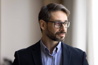 Düşünceli, orta yaşlı, şık gözlüklü bir iş adamı pencereden dışarı bakıyor, mesleki meydan okuma, şirket başarısı, liderlik, gelecek projelerini planlıyor.
