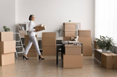 Yaşlı kadın depo müdürü ya da lojistik koordinatörü istiflenmiş paketlerle dolu odalarda karton kutular taşıyor, çalışma alanındaki paketleme, etiketleme ve paketleme işlemlerine katılıyor.