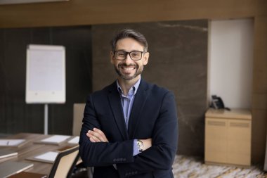Şık ceketli ve gözlüklü, elleri katlanmış, gülümseyen ofis yönetim kurulu odasında duran profesyonel portre için poz veren mutlu İspanyol şirket CEO 'su. İş vesikalığı