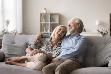 Neşeli olgun karı koca kanepede birlikte dinleniyor, sarılıyor, konuşuyor ve gülüyor birlikte eğleniyor, şakalaşıyor, eğleniyor, armoni ilişkilerinin tadını çıkarıyor, anlayış ve ortak espri anlayışları.