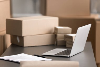 Sevkiyatları işlemek, nakliyeyi yönetmek, depolamak, siparişleri ya da lojistiği organize etmek için ev içi depo çalışma alanı. Masanın üstündeki dizüstü bilgisayarı kapat. Yakınlarda çeşitli boyutlarda karton kutular var.