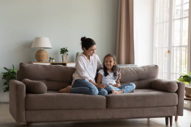 Genç Hintli anne anaokulu çocuğu güzel kızını kucaklıyor kanepeye oturuyor, sevgi dolu aile sıcak sohbetin ve modern evde güvenilir konuşmaların tadını çıkarıyor. Yetiştirme, velayet ve iletişim kavramı