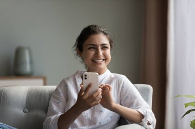 Arama yap, iletişim kurma ve e-servis alıcısı, modern kablosuz teknoloji kullanımı kavramı. Gülümseyen neşeli Hintli kadın akıllı telefon kullanarak evde dinleniyor, online sohbetin veya çöpçatanlık hizmetlerinin keyfini çıkarıyor.