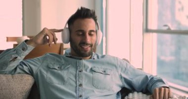 Kablosuz kulaklıklı mutlu Latin adam ev koltuğunda dinleniyor, kapalı gözlerle müzik dinliyor, favori melodilerden, şarkılardan, podcast 'ten, kulaklıklardan hoşlanıyor.