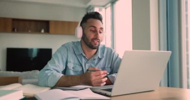 Yakışıklı, genç, kulaklıklı Latin bir öğrenci öğretmenle, sınıfla, video konferansında, laptopta konuşuyor, ders çalışmak için açık kitaplarla çalışıyor.
