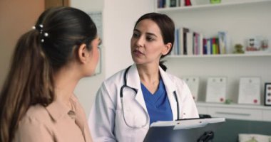 Hastalık belirtileri hakkında soru soran kadın doktor. Özel klinikteki genel sağlık kontrolüne gelen genç kadın hastaya durumu. Sağlık, profesyonel sağlık hizmetleri, sağlık sigortası.