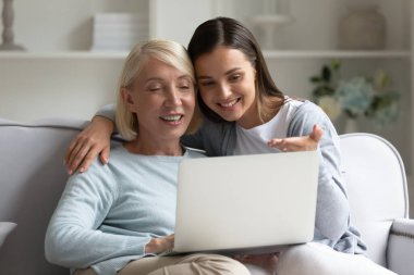 Mutlu yetişkin anne ve kız dizüstü bilgisayar kullanıyor, internette sörf yapıyor ya da internetten alışveriş yapıyor, büyük anne ve torun bilgisayar ekranlarına bakıyor, video veya film izliyor, evde eğleniyor.
