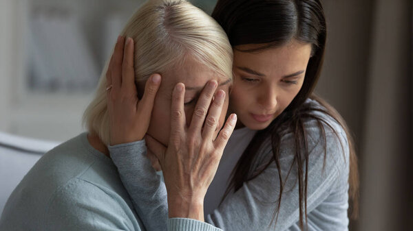 Caring daughter embracing, comforting soothing unhappy crying mature mother close up, helping to overcome problems, loving granddaughter cuddling supporting stressed older grandmother