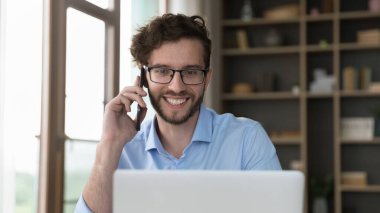 Gözlüklü gülümseyen adam dizüstü bilgisayar ekranına bakıyor. Akıllı telefon başında gayri resmi konuşma yapıyor. İç işleri masasında oturuyor, işi uzaktan çözüyor, online alışverişi tartışıyor, müşteri hizmetleri müdürüyle konuşuyor.