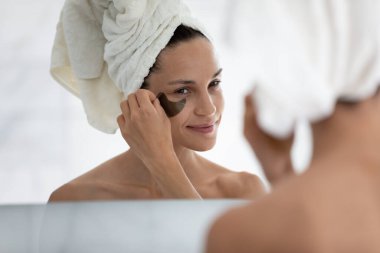 Banyodaki aynaya baktıktan sonra genç ve güzel bir kadın göz jeli bantlarının altına başvurur, milenyum kızı her sabah banyo, yüz kozmetolojisi, cilt bakımı, yüz bakımı...
