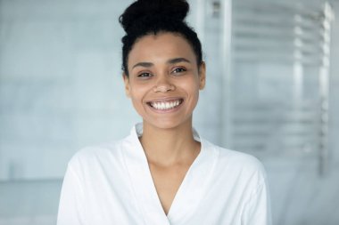 Gülümseyen Afrikalı Amerikan milenyum kızı banyodan sonra banyoda poz verirken çekilmiş bir portre. Ev banyosunda yüzü parlayan sağlıklı melez bir genç kadın.