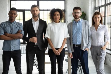 Gelecek vaat eden genç iş arkadaşlarının toplu portresi. İşteki kendine güvenen şirket çalışanları bir arada duruyor ve kameraya bakıyor. Modern çalışma alanındaki çok uluslu organizasyonun personel üyeleri