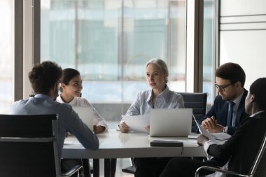 Yaşlı kadın yönetici çeşitli personele ders veriyor, yönetim kurulunda grup toplantısına katılıyor, analiz ediyor, evrak teftişi yapıyor, pazarlama planını geliştiriyor, brifingdeki işçilere yeni stratejiyi anlatıyor.