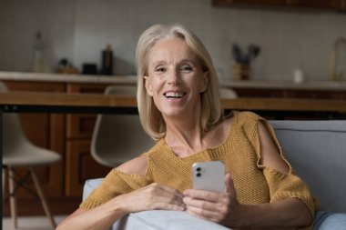 Mutlu orta yaşlı kadın kanepede dinleniyor, internette boş zaman geçiriyor modern akıllı telefonlara bakıyor kameraya bakıyor rahat bir hayat için teknolojiden keyif alıyor. E-servis, e-alışveriş müşteri portresi konsepti