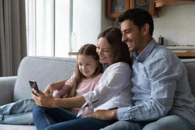 Fotoğraf çek, fotoğraf çek, cep telefonuyla aile fotoğrafı çek, modern teknoloji kavramı. Çift ve kızı hafta sonunu evde oturup akıllı telefon kullanarak yurt dışında yaşayan akrabalarıyla video konferansı yaparak geçirirler.