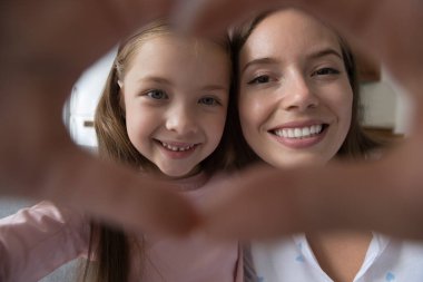 Anne ve kızının sevimli yüzleri kalp simgesi gösteren parmakları birleştirir, kırpılmış atışları kapatır. Anneler Günün kutlu olsun, koşulsuz sevgi, blog yazarları video kaydı, aile paylaşımı samimi duygular, video çağrı konsepti