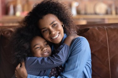 Gülümseyen Afrikalı Amerikalı anne, küçük kızını kucaklıyor, uzaktan bakıyor, mutlu bir anne ve güzel bir gelecek hayal ediyor.