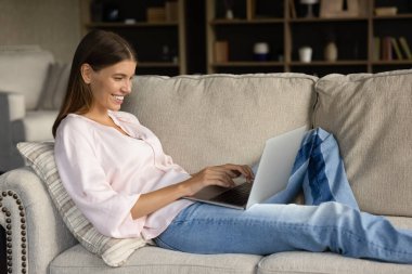 Mutlu genç bir kadın rahat koltukta dinleniyor, dizüstü bilgisayar kullanıyor, daktilo çekiyor, ekrana bakıyor, gülümsüyor, gülüyor. Neşeli kız internette sohbet ediyor, mesajları okuyor, internette geziniyor.