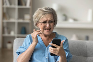 Akıllı telefona bakarken tatminsizlik ya da hayal kırıklığı yaşayan yaşlı bir kadın, teknik sorunlar, düşük arama kalitesi, düşük bağlantı, e-posta okuma ya da kötü haber içeren mesaj