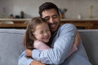 Sevgi dolu küçük kız sevgili babacığını yanak teması, kapalı gözler, mutlu ve şefkatli babacığa sarılıyor, gülüyor, gülümsüyor. Baba kucağında tatlı bir kız çocuğu