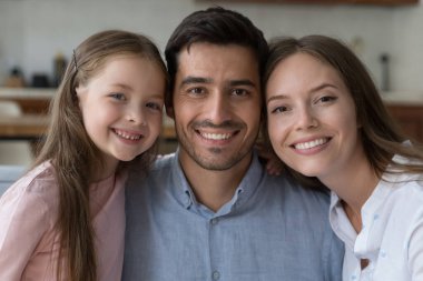 Mutlu, çekici bir çift ebeveyn ve güzel küçük kız çocuk portresi. Genç anne, baba, çocuk kız kameraya dişlek gülümsemeyle bakıyor, yakın oturuyor, sarılıyor. Aile kavramı