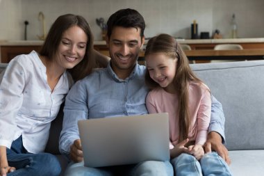 Mutlu küçük çocuk, annesi ve babası film izlerken, İnternet TV kanalı laptopta, alışveriş yaparken, video konuşmasında, bilgisayar aleti kullanırken, ekrana bakarken, gülerken, kanepede dinlenirken,