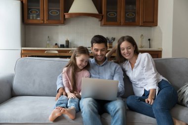Neşeli, gülen bir çift ebeveyn ve küçük çocuk online uygulamayı dizüstü bilgisayarda kullanıyor, koltukta dinleniyor, film izliyor, program yayıncılığını eğlendiriyor, interaktif TV seyrediyor. İletişim konsepti