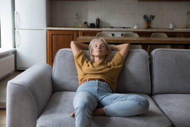 Huzurlu orta yaşlı ev sahibi kadın evdeki rahat koltukta gözleri kapalı dinleniyor, temiz havayı ihlal ediyor, gündüzleri uyuyor, meditasyon yapıyor, keyfine bakıyor, rutinini bozuyor.