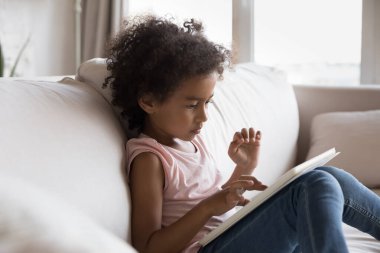 Şirin 5 'li kıvırcık saçlı Afrikalı kız dijital tablet kullanarak evde tek başına oturup oyun oynuyor. Genç nesil modern kablosuz teknolojiler aşırı kullanım kavramı