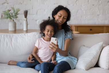 Sevimli Afrikalı anaokulu kızı annesi akıllı telefon uygulaması yapıyor evde koltukta oturup iletişimi, oyunu, eğitici veya eğlenceli içerikleri izlemeyi seviyor. Teknoloji, eğlenceli konsept