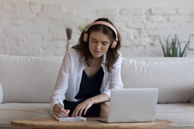 Kendi kendini eğitme, interneti kullanarak bilgiyi geliştirme, çevrimiçi etkin çalışma, e-öğrenme, modern teknoloji konsepti. Kulaklıklı genç bayan kursu dinle, işine odaklan evdeki kanepeye otur ve dizüstü bilgisayarı kullan.