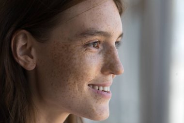 Yan görünüşlü çekici bir kadın yüzü, çillerle kaplı pürüzsüz bir ten, hayal kuran bir kadına bakan bir kadın, yakın çekim görüntüsünden zevk alıyor. Görüş, görme bakımı, gençlik konsepti