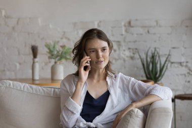 20 'li yaşlarda çilli bir kadın koltukta oturup akıllı bir telefonla konuşuyor. Cep telefonu bağlantısı kullanan aile ya da arkadaşlarıyla uzaktan konuşuyor. Mesafeli iletişim, modern teknoloji, telefon görüşmesi konsepti