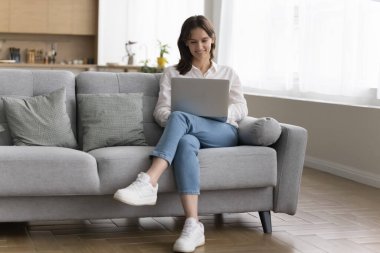 Tasasız genç kadın hafta sonunu evde dizüstü bilgisayarla geçiriyor, oturma odasında serbest çalışıyor, internette sörf yapıyor, mesaj atıyor, alışveriş yapıyor, bilgisayar başında çalışıyor, e-postaları kontrol ediyor, önemli bilgileri araştırıyor.