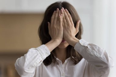 Close up head shot portrait young woman hides her face behind palms feels ashamed, shy or afraid pose indoor. No see, ignoring, dont listen to slander, gossips, try to cope with emotional breakdown clipart