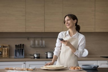 Neşeli ev hanımları mutfakta yemek pişirir ve modern akıllı telefonlar kullanır, internette sohbet eder, yemek tarifi hazırlar, sosyal ağlar için İtalyan mutfağının fotoğrafını çeker, evde yemek pişirmenin ve hobilerin tadını çıkarır.