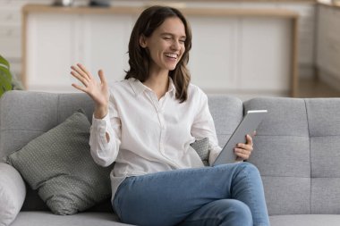 Mutlu genç kadın oturma odasındaki kanepede rahatla dijital tablet tut, sanal aile sohbeti yap modern uygulamaları kullan, video görüşmeleri yap, gülümse, mesafeli iletişimin tadını çıkar