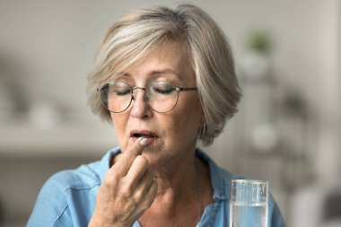 Kapalı yaşlı kadın ilaç ve bir bardak su alır, ilaç alır, sağlığını korur, kronik ağrı veya eklem iltihabını kontrol eder, osteoporozu önlemek için kalsiyum ve vitamin alır, daha düşük kolesterol seviyesi, sağlıkla ilgilenir.