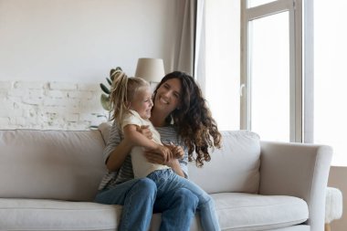 Genç, neşeli İspanyol kadın, sevimli anaokulu 5 'li kızıyla oynaşıyor, modern oturma odasında birlikte eğleniyor, çok mutlu oluyor. Aile eğlencesi, evde oyunlar, mutlu annelik, evlat edinme kavramı.