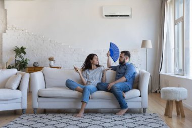 Kadın uzaktan kumandayı çalıştırıyor, kocası klimayı açıyor, kağıt vantilatör kullanıyor, tartışıyor, bozuk havalandırma sisteminden memnun değil, kavga ediyor, pahalı elektrik kullanıyor, faturalardan tasarruf etme ihtiyacı duyuyor.