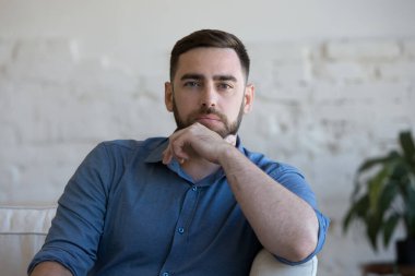 Düşünceli milenyum adamı oturma odasında kanepede oturup kameraya bakıyor. Yakışıklı bekar bir adamın profil fotoğrafı evde tek başına dinlenerek zaman harcıyor. Kiracılık, genç ev sahibi veya kiracı portresi konsepti