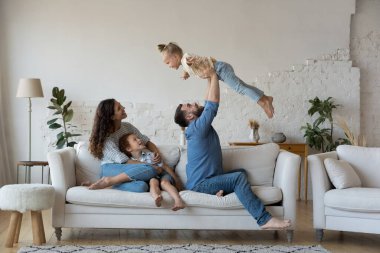 Çocuklu bir çift oturma odasında bir araya toplanmış, birlikte oynuyorlar kanepeye oturuyorlar, sevgi dolu baba kollarını kaldırıyor tatlı kız, anne ve oğlu kanepede dinleniyorlar. Ev kavramında iyi bir aile hafta sonu.