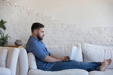 Ciddi serbest çalışan bir adam kanepeye oturur dizüstü bilgisayarla uzaktan müşteriye e-posta, daktilo cevapları, iş adamının işi evden çözmesi yoluyla karşılık gelir. Modern teknoloji, tele çalışma kavramı