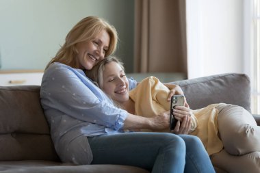 Neşeli orta yaşlı anne ve genç yetişkin kız telefonda video konuşmaları, akıllı telefonda dinlenme, sevgi, özen, bağlılık, aile eğlencesi