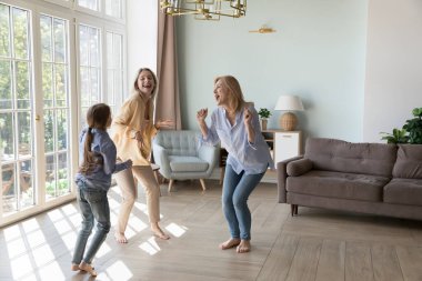 Mutlu genç anne, kız çocuk, enerjik büyükanne birlikte dans ediyor, şarkılar söylüyor, aile partisinden zevk alıyor, aktivite, boş zaman, anneler gününü kutluyor, oturma odasında 8 yürüyüş.