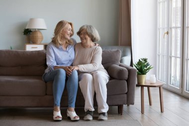 Mutlu yetişkin bir kız, yaşlı bir anneyi ziyaret ediyor, evde vakit geçiriyor, konuşuyor, gülüyor, sevgiyle, özenle, sevgiyle yaşlı anneyi kucaklıyor. Tam boy portre